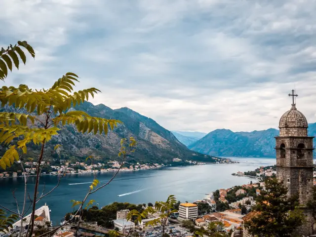 Blick auf die Bucht von Kotor, Montenegro, mit einem Kirchturm im Vordergrund und Bergen im Hintergrund.