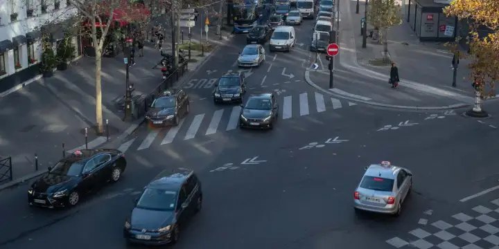 Verkehr in Paris: Autos und Taxis auf dem Weg zum Ziel. Ein silbernes Taxi fährt über den Zebrastreifen, während andere Fahrzeuge im Stau stehen.