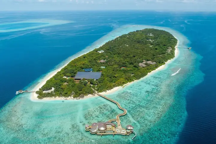 Soneva Fushi: üppige Insel mit Villen, Solaranlagen und einem Steg zu einem Restaurant im türkisfarbenen Wasser.